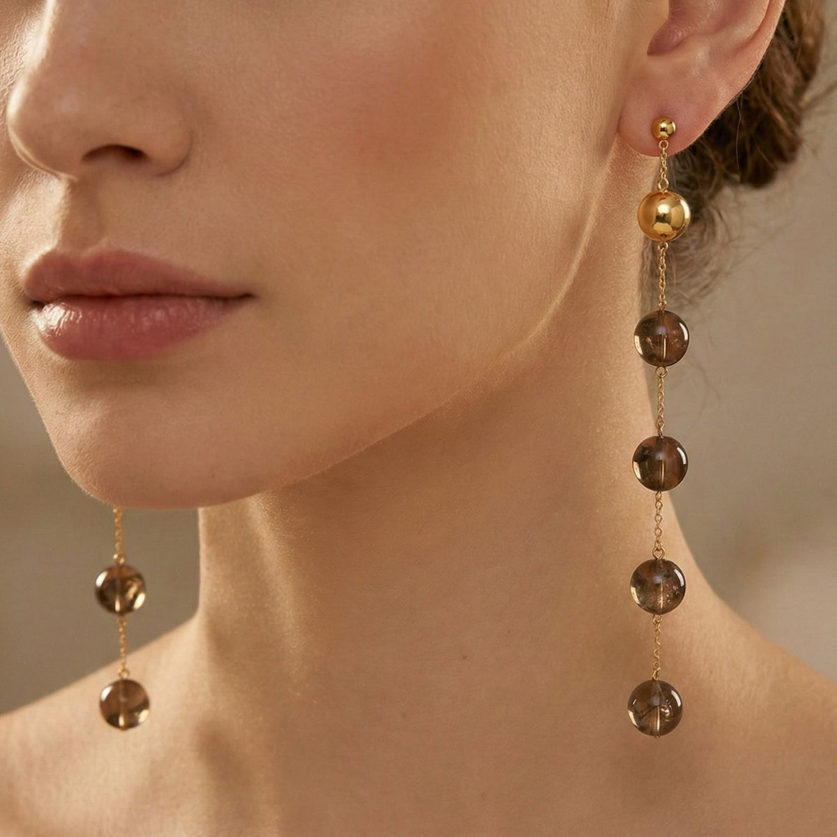 A close-up of a woman's lower face and neck showcases JAREDJAMIN Jewelry Online's Nora Dangle Smoky Quartz Earrings, crafted in 18k gold with five smoky quartz beads each, elegantly contrasting her fair skin and natural lips.