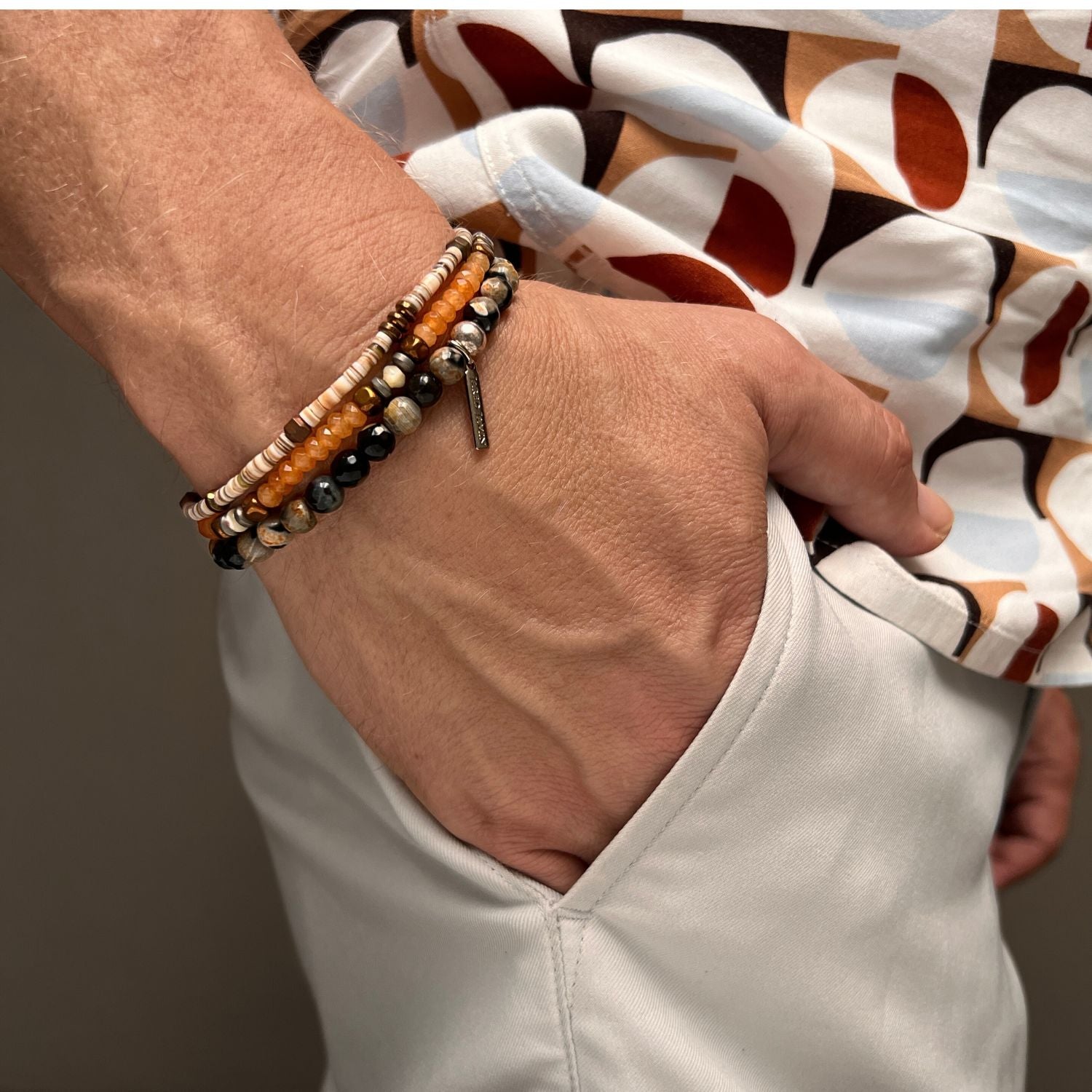 The Orange Tiger Bracelet Set by JAREDJAMIN Jewelry Online features a coiled design with small round beads in orange, brown, white, and copper tones, accented by agate. It wraps multiple times with a brown leather loop for secure fastening.