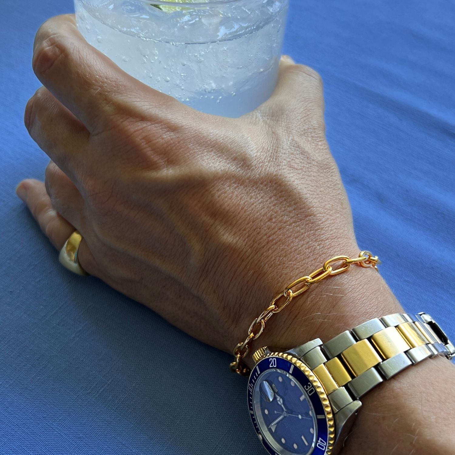 The Gold Chain Reaction Bracelet by JAREDJAMIN Jewelry Online features 18K gold plating, elongated oval links, a round clasp, and a rectangular engraved tag. Shown against a white background.