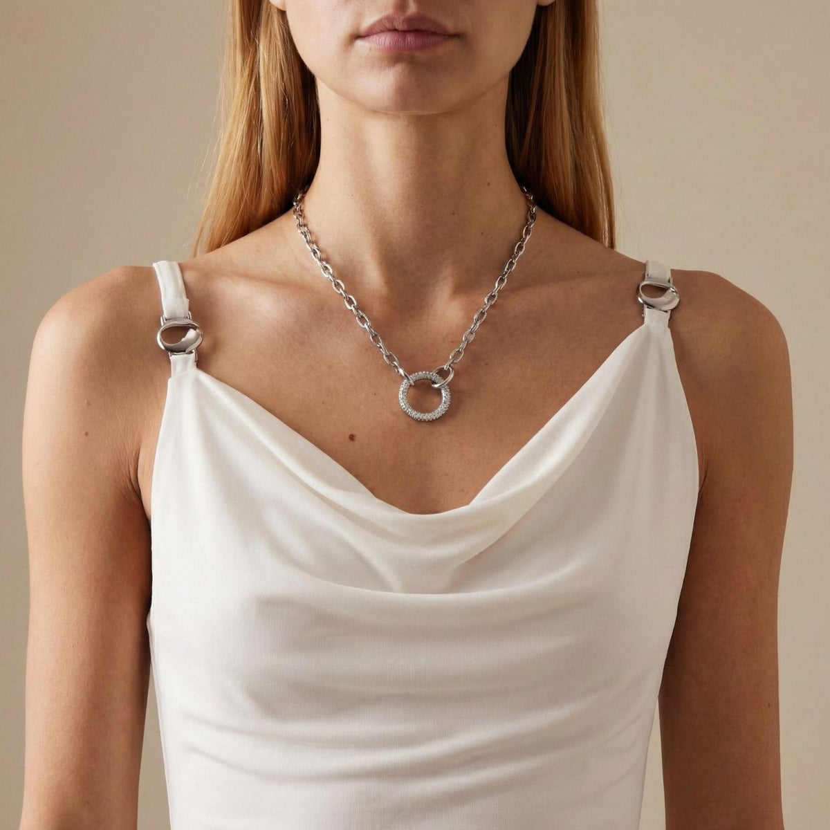 A woman wears a sleeveless white cowl-neck top with silver ring-strap details, paired with the 18" Reaction Circular Pave Clasp Necklace from JAREDJAMIN Jewelry Online. A plain, neutral background keeps focus on her upper body and jewelry.