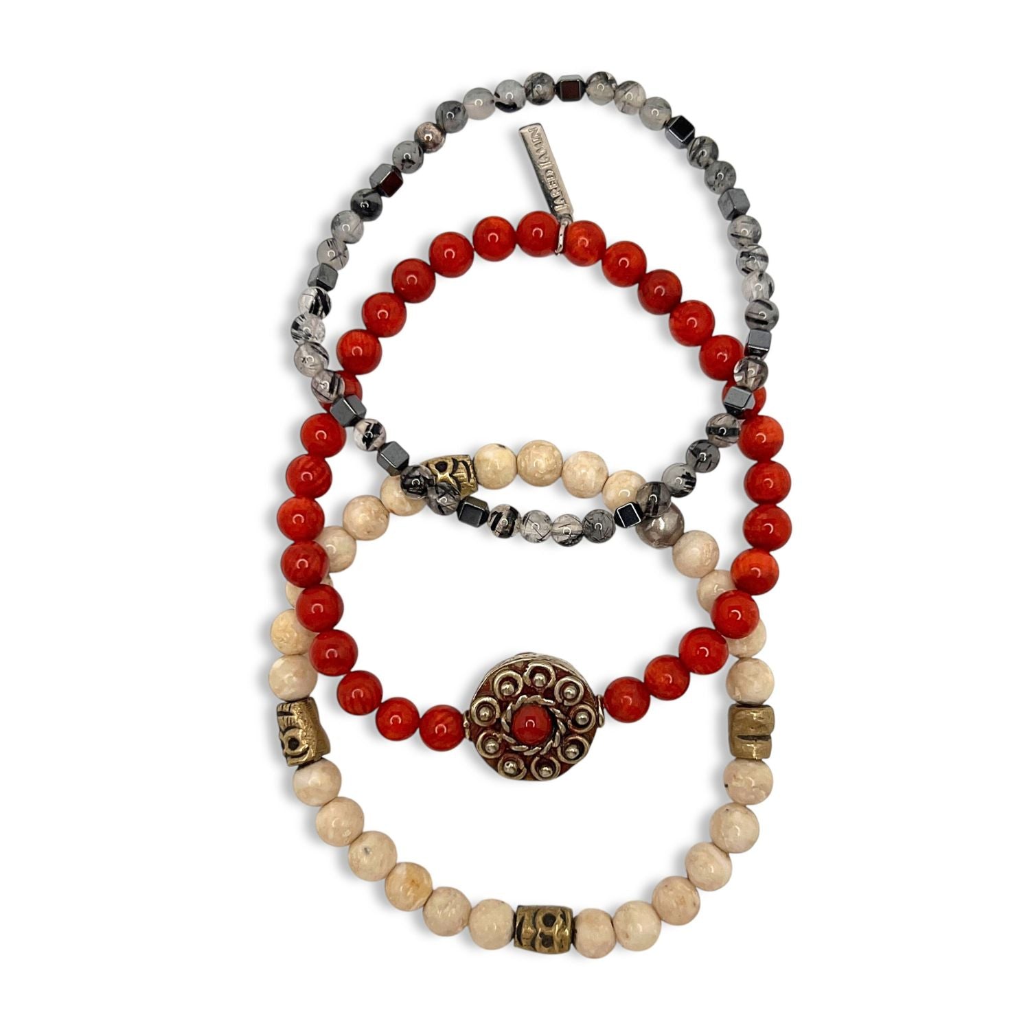 The Red Barron Bracelet Set from JAREDJAMIN Jewelry Online includes three stackable bracelets: marbled black and white beads with a metal tag, coral beads with a metal skull, and cream beads with Tibetan spacers and a red-centered charm.