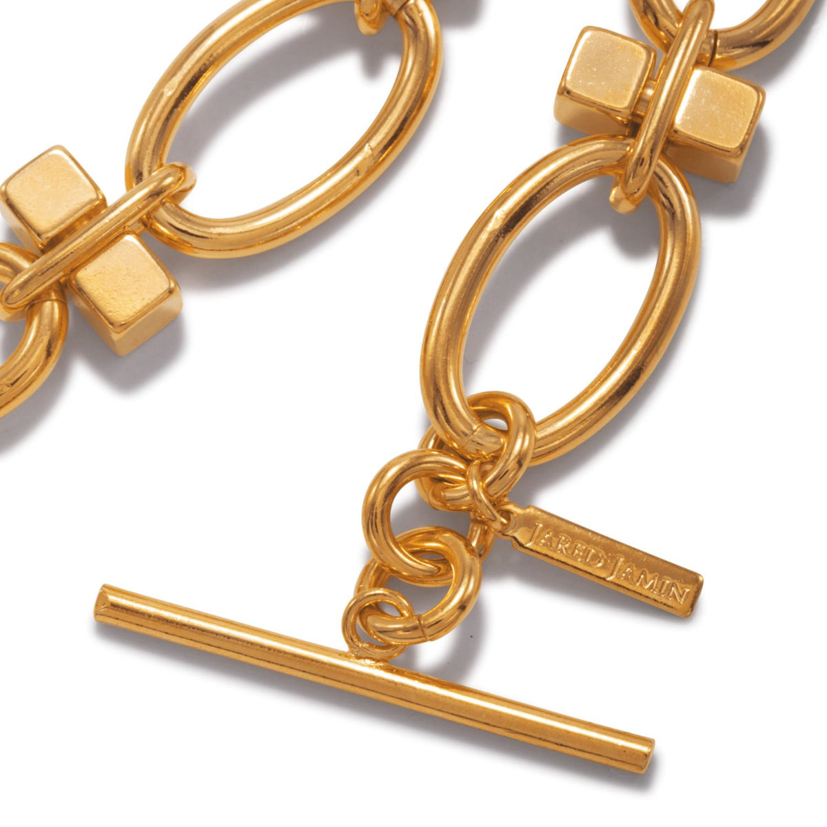 Close-up of the Reign Gold Link Bracelet by JAREDJAMIN Jewelry Online, featuring large 18K gold-plated oval links with square accents and an adjustable toggle clasp with a branded tag, shining against a white background.