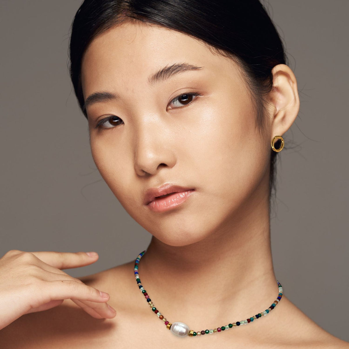 A young woman with smooth skin and straight dark hair poses against a neutral background, wearing JAREDJAMIN Jewelry Online’s Rowan Necklace Multi Color Necklace—an adjustable freshwater pearl piece with multi-colored faceted beads.