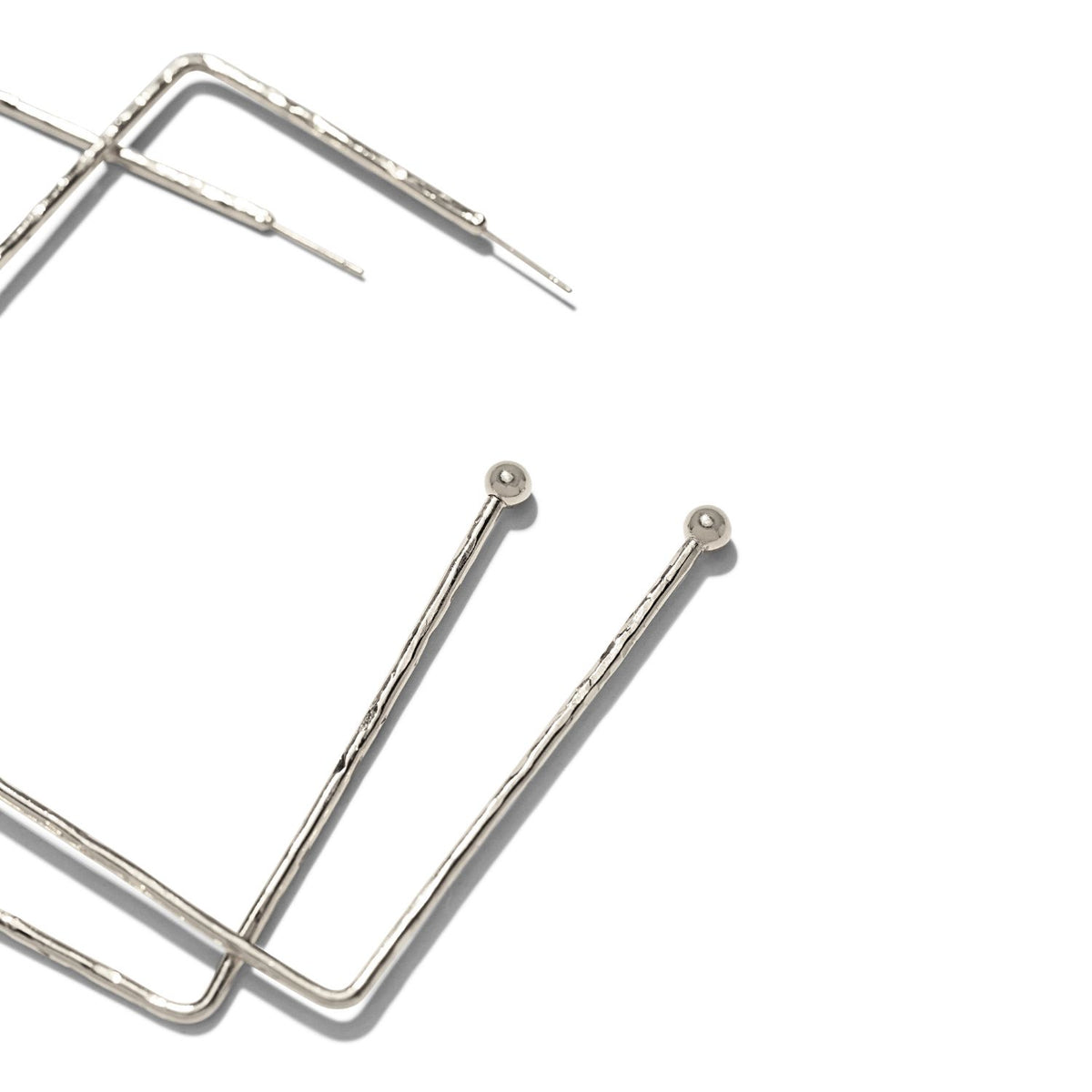 Close-up of two thin, silver Silver Squaretastic Hoop Post Earrings by JAREDJAMIN Jewelry Online, featuring L-shaped hammered hoops with small round loops at the tips and a wavy texture, set against a white background.