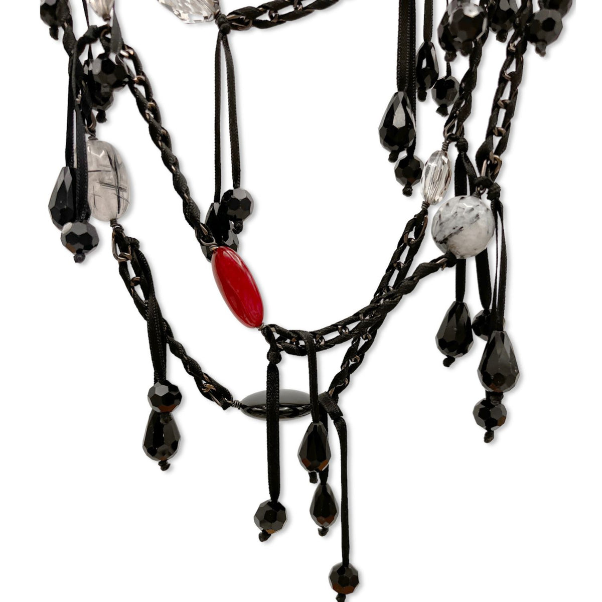 The See You Saloon Necklace by JAREDJAMIN Jewelry Online features gunmetal chain links, black ribbon, assorted black, clear, and marbled beads, a large red oval accent, and dangling quartz teardrops for a bold layered look.