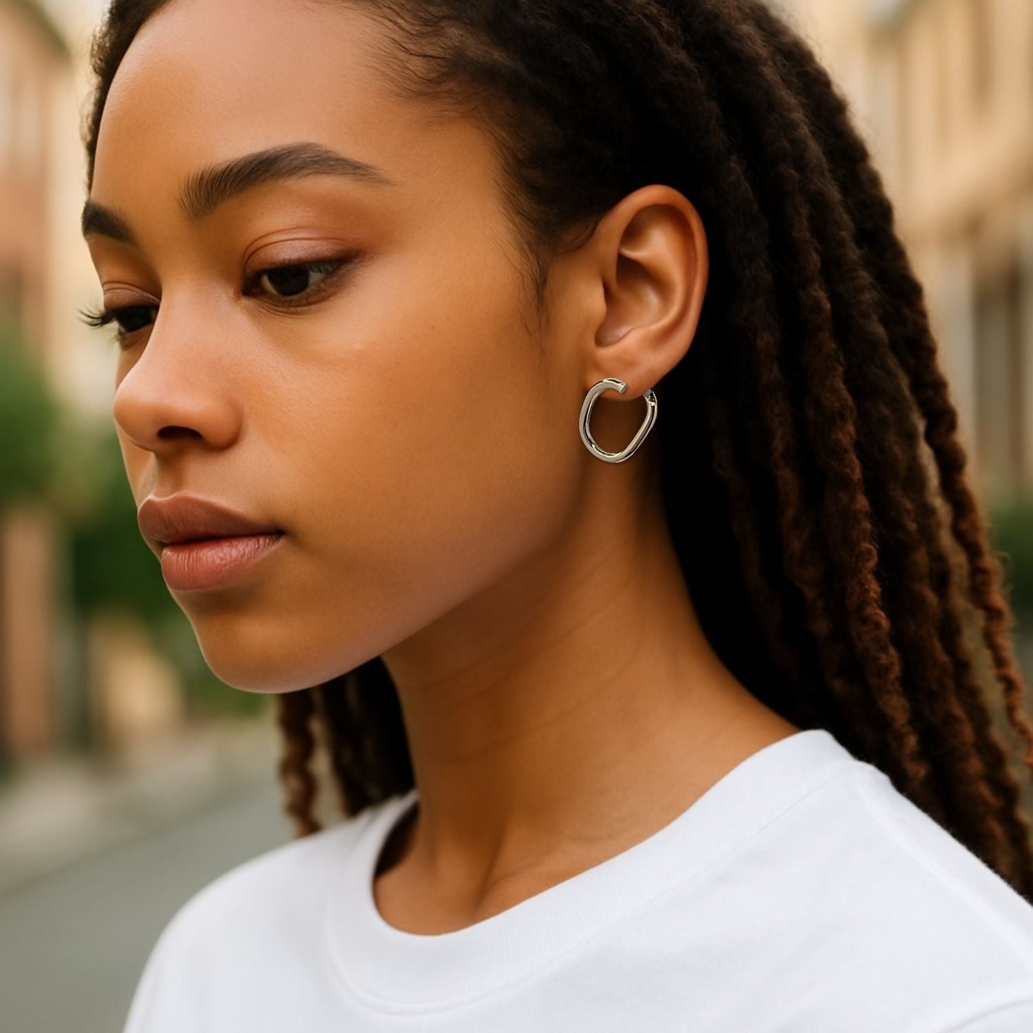 The Silver Billie Stud Post Earrings by JAREDJAMIN Jewelry Online are small, chunky silver hoops with a smooth, polished finish and an irregular oval shape, shown on a white background casting soft right-side shadows for an edgy statement.