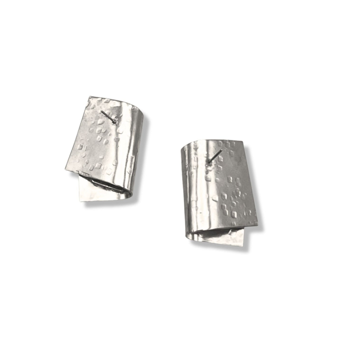 The Silver Fold Over Post Earrings by JAREDJAMIN Jewelry Online feature uniquely folded, rectangular silver-plated designs with a crumpled texture and dotted patterns, creating an asymmetrical, architectural look. Shown on a plain white background.