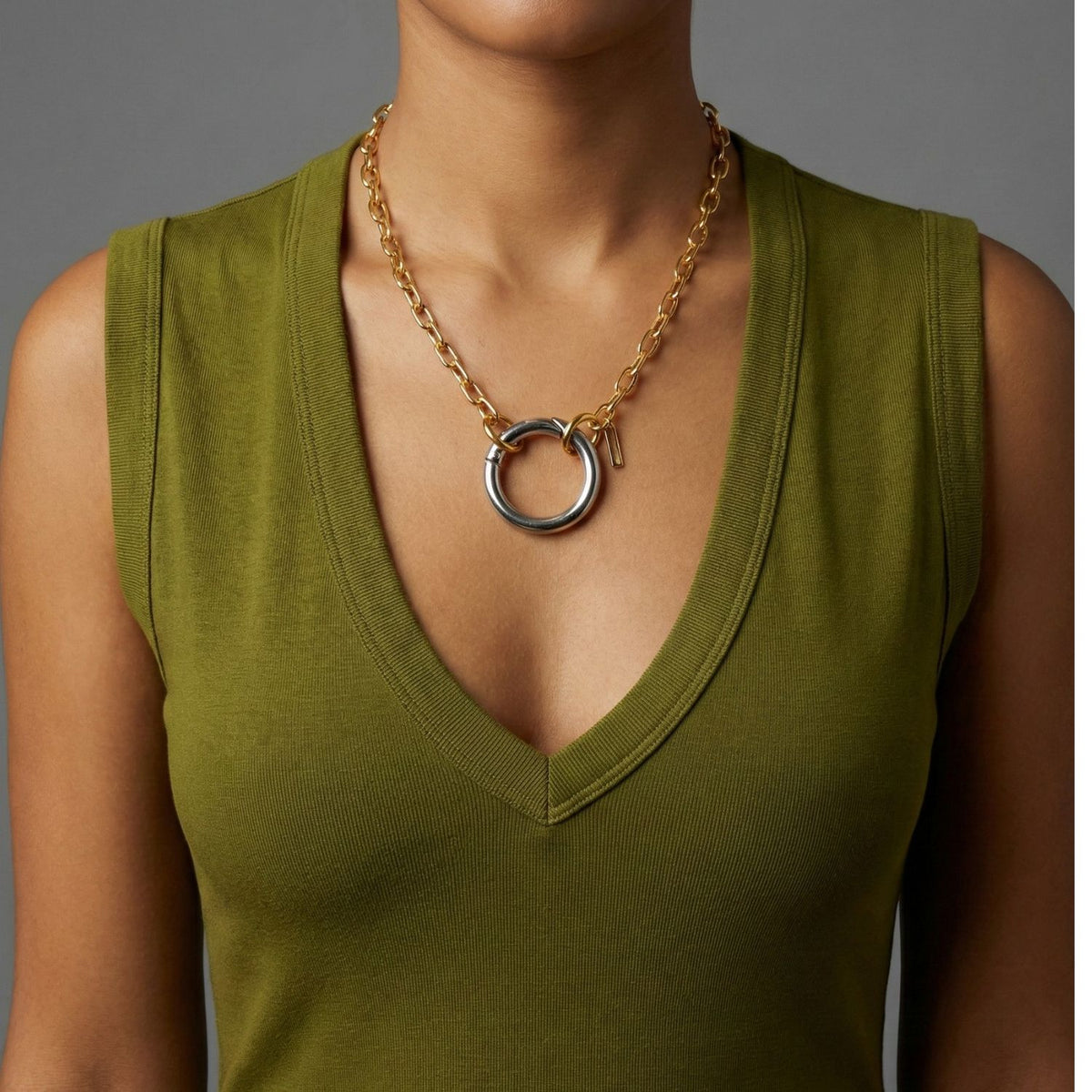 An individual models the JAREDJAMIN Jewelry Online Silver Large Circular Clicker Clasp necklace, styled with an olive green sleeveless deep V-neck top, against a plain gray background. The person's face is not shown.