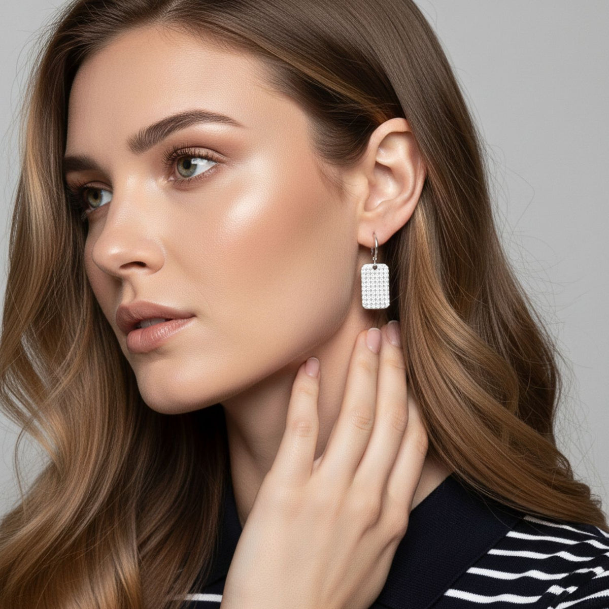 Un woman avec wavy light brown hair et glowing skin gazes left, wearing a black et white striped top. She shows off JAREDJAMIN Bijoux en Ligne’s argent Robin Pave breloque créole boucles d'oreilles—perfect for everyday style—against a plain light gray background.