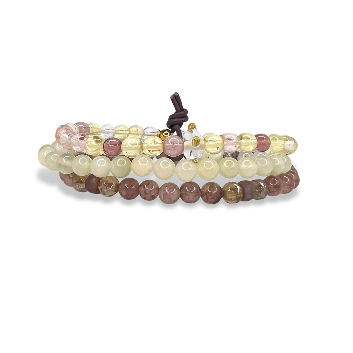 The Sunset Quarry Bracelet Set by JAREDJAMIN Jewelry Online features three layers of coiled round beads in pastel yellow, pink, clear, and mauve with a brown leather knot fastening and a smooth, polished finish.