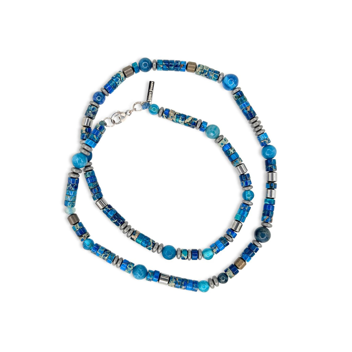 The Sur Side Jasper Beaded Necklace by JAREDJAMIN Jewelry Online features blue and silver cylindrical, round, square, faceted agate beads, and silver-plated hematite. Coiled in an oval on white, it showcases detailed beadwork and a metal clasp.