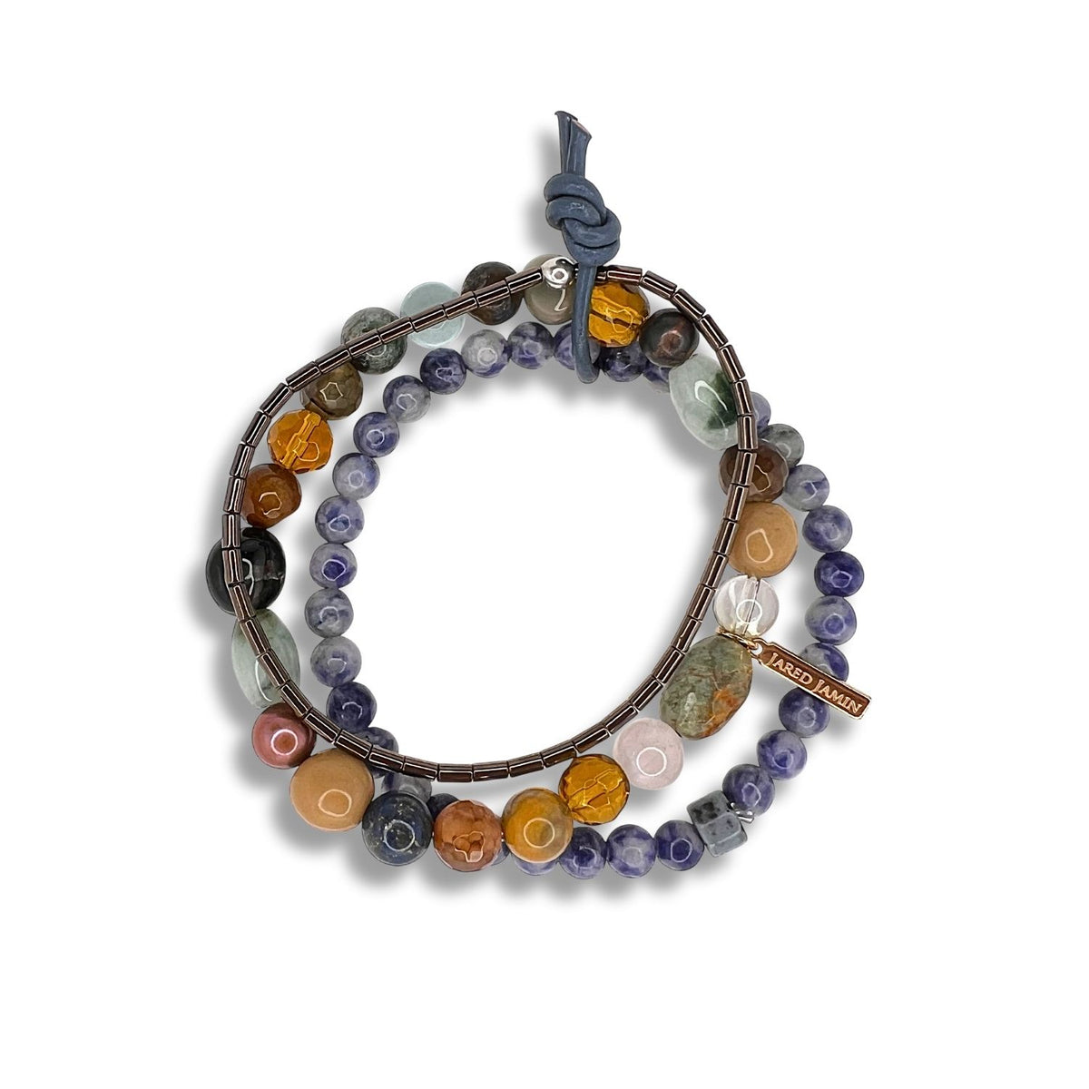 The Uptown Dream Bracelet Set by JAREDJAMIN Jewelry Online features multicolored stone and glass beads in earth tones, a knotted blue leather cord, a metal “JARED MADE” tag, and a stone charm—coiled elegantly in a circle.