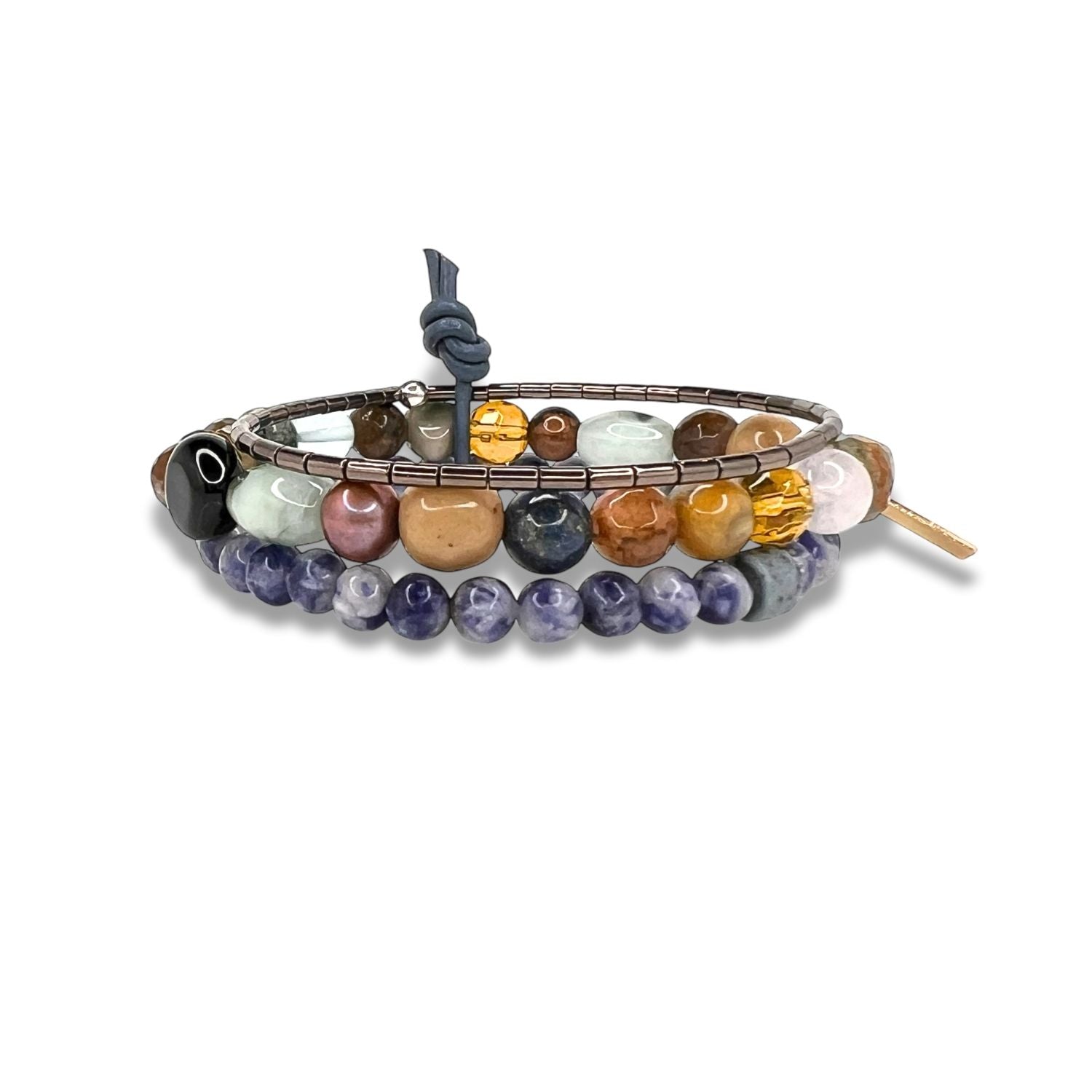 The Uptown Dream Bracelet Set by JAREDJAMIN Jewelry Online features a stylish stack of beaded bracelets in blue, purple, brown, green, amber, and pink stones, including sodalite and sleek hematite, finished with a cord knot and metal tag.