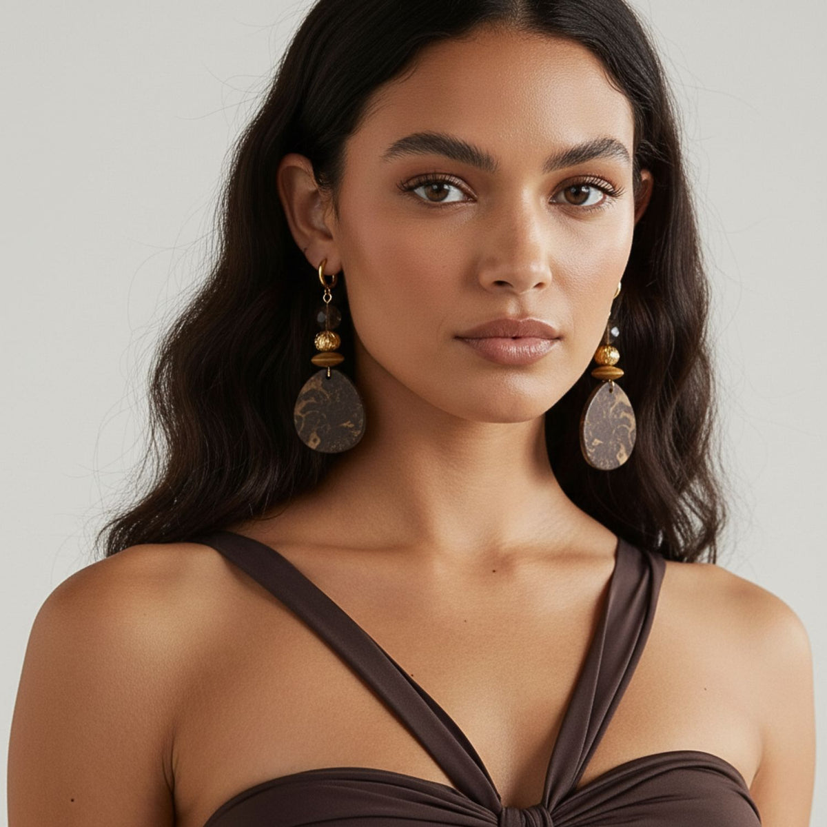 Un woman avec long, wavy dark hair wears JAREDJAMIN Bijoux en Ligne's Velvet Drops Jasper boucles d'oreilles—large, round imposant pieces avec plaqué or accents. She looks at the camera neutrally, set against a plain light gray background.