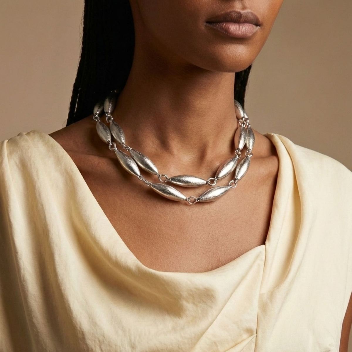 Los Zeppelin Phoebe plata collar de JAREDJAMIN shines con artisanal, small-batch craftsmanship in West Hollywood. Sustainable de lujo con a brushed plata finish y distinct signature texture, mostrado sobre a model en un cream draped top against a neutral backdrop.