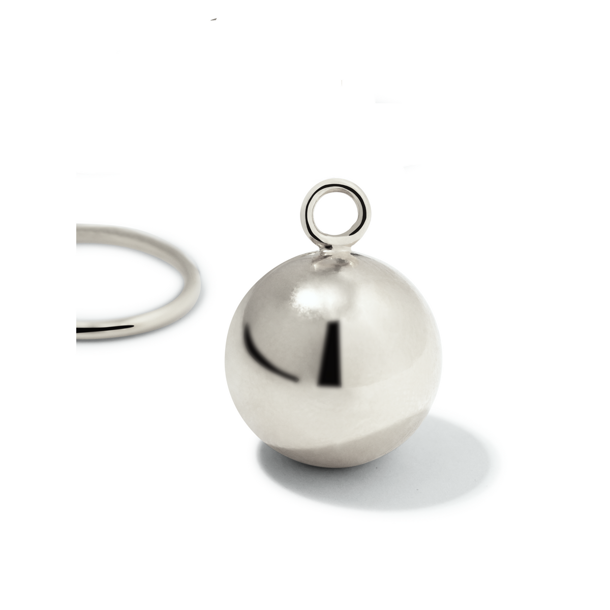 Un plata Orbita Ball dije Click-Top aro pendiente de JAREDJAMIN Joyería Online rests sobre un fondo blanco, its brillante dije con a small loop catching the light. To the left, part of another pendiente casts a subtle shadow in the minimal scene.