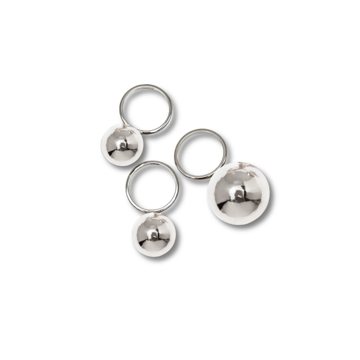 Los Orbita plata Three anillo Stack de JAREDJAMIN Joyería Online features brillante plata-plated anillos con reflective spheres in varying sizes, artfully scattered sobre un fondo blanco y casting soft gray shadows.