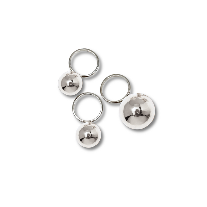 The Orbita Silver Three Ring Stack by JAREDJAMIN Jewelry Online features shiny silver-plated rings with reflective spheres in varying sizes, artfully scattered on a white background and casting soft gray shadows.