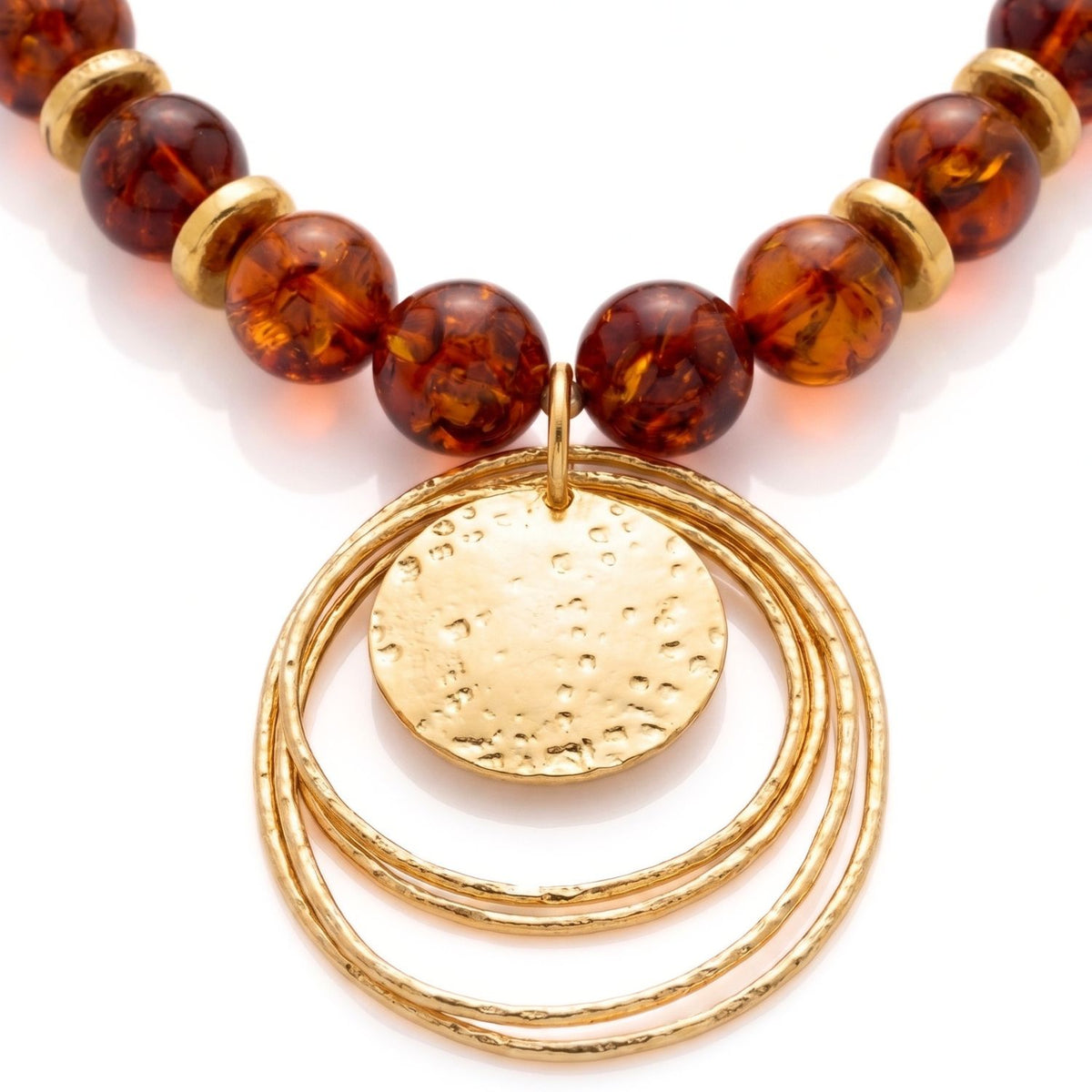 Close-up detail of the Jared Jamin Peacock Dawn necklace, highlighting the intricate hand-hammered texture of the 18K gold-plated concentric circles and the deep, honey-toned glow of the natural amber gemstones.