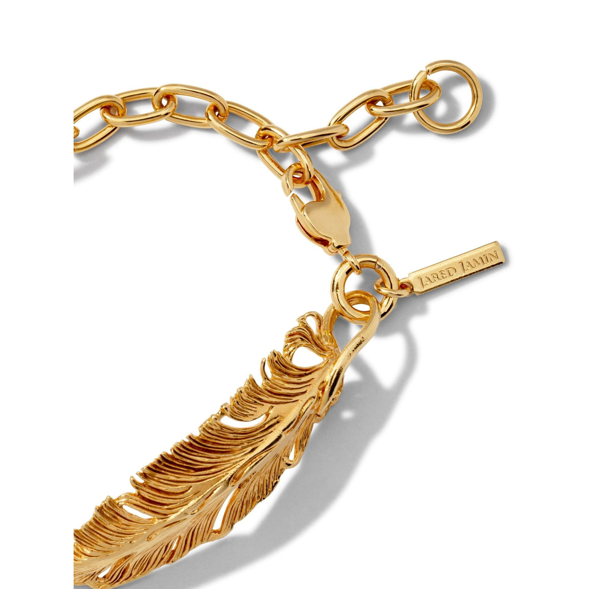 Close-up of the Gold Feather Plume Bracelet by JAREDJAMIN Jewelry Online, featuring oval chain links, a detailed feather-shaped pendant, and a lobster clasp with a tag engraved "JAREDJAMIN" for an elegant, polished finish.