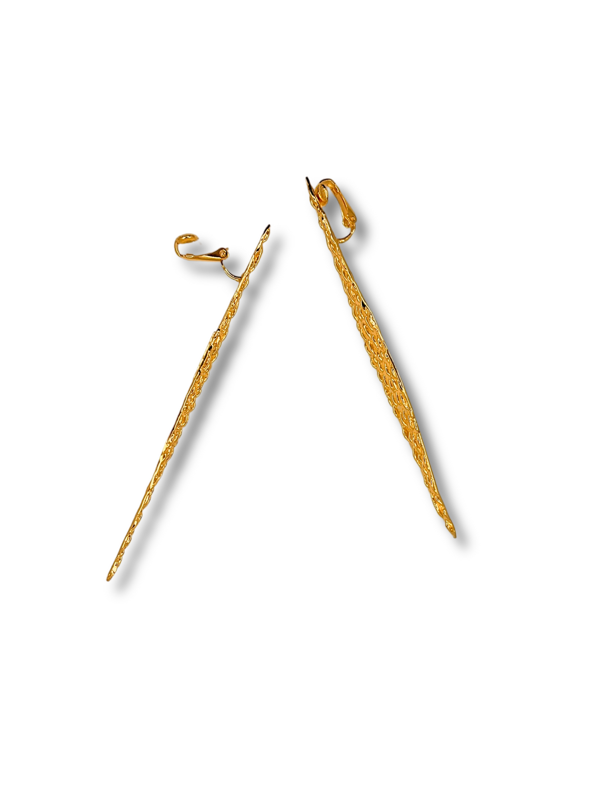 The Jaguaretê Earrings by JAREDJAMIN Jewelry Online are long 18K gold earrings with a narrow, tapered design. One earring lays flat, revealing its full length, while the other stands upright to display the hook clasp. Their abstract form and textured finish cast soft shadows on the white background.