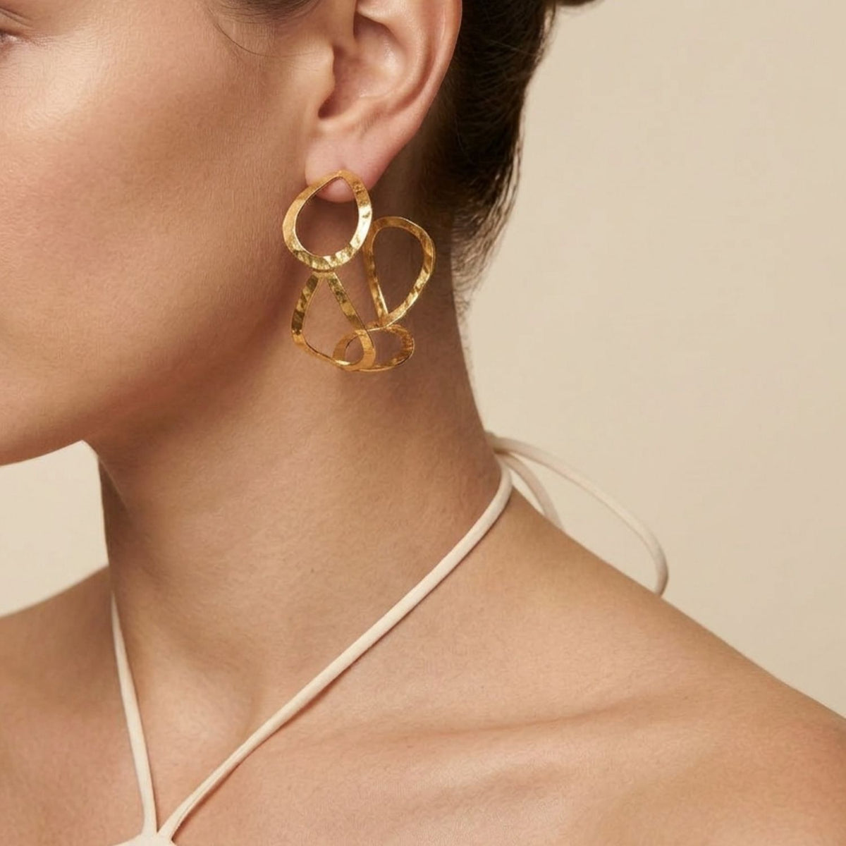 Close-up profile portrait of a female model wearing a white halter top and the 2 1/4-inch Julia Hoop Post Earrings, demonstrating the bold, open-air architectural teardrop silhouette framing the jawline.