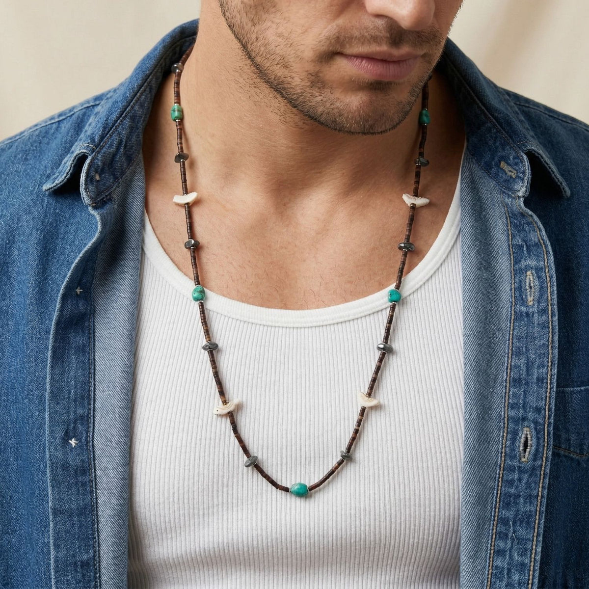 Close-up portrait view of a male model wearing the 32-inch Kai Multi-Mineral Necklace over a white ribbed tank top and an unbuttoned blue denim shirt, illustrating its long, relaxed visual drape and organic color contrast.