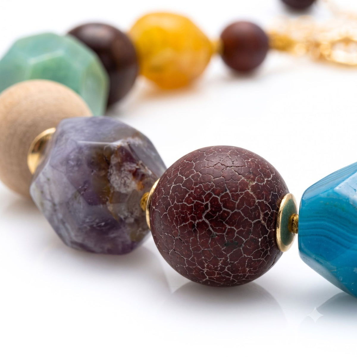 Close-up studio macro shot focusing on the hand-knotted mixed-media beads—including crackled agate, faceted amethyst, and natural wood—separated by 18k gold-plated metal bead caps.