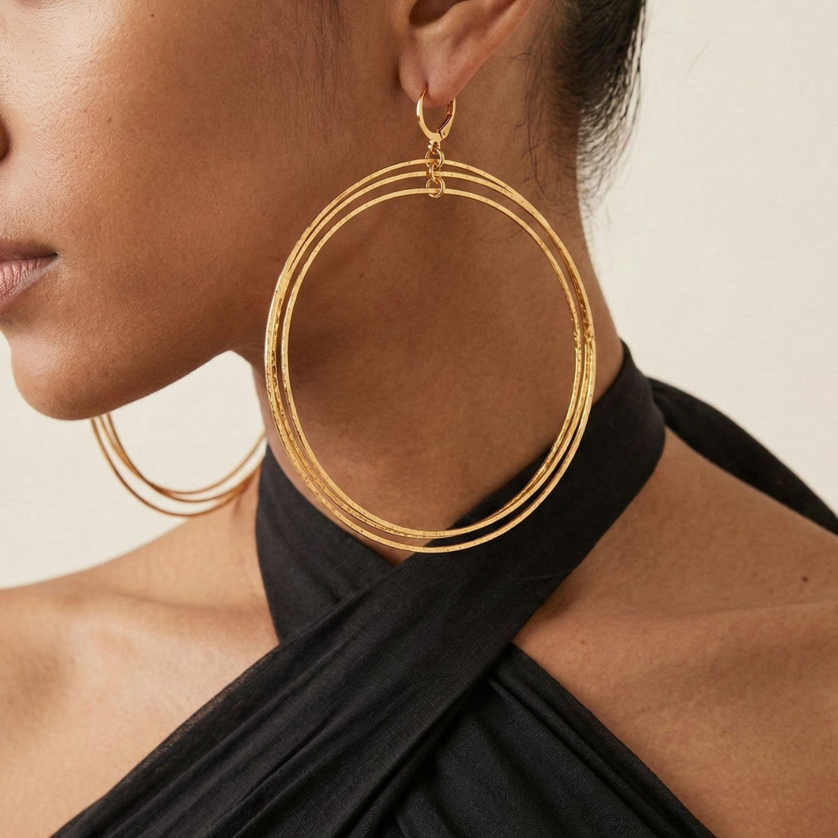 Close-up of a person wearing JAREDJAMIN Jewelry Online Gold Triple Halo Hoop Earrings with a black halter-neck top. The cropped image highlights the earrings, showing only the lower half of the face, ear, neck, and shoulder.