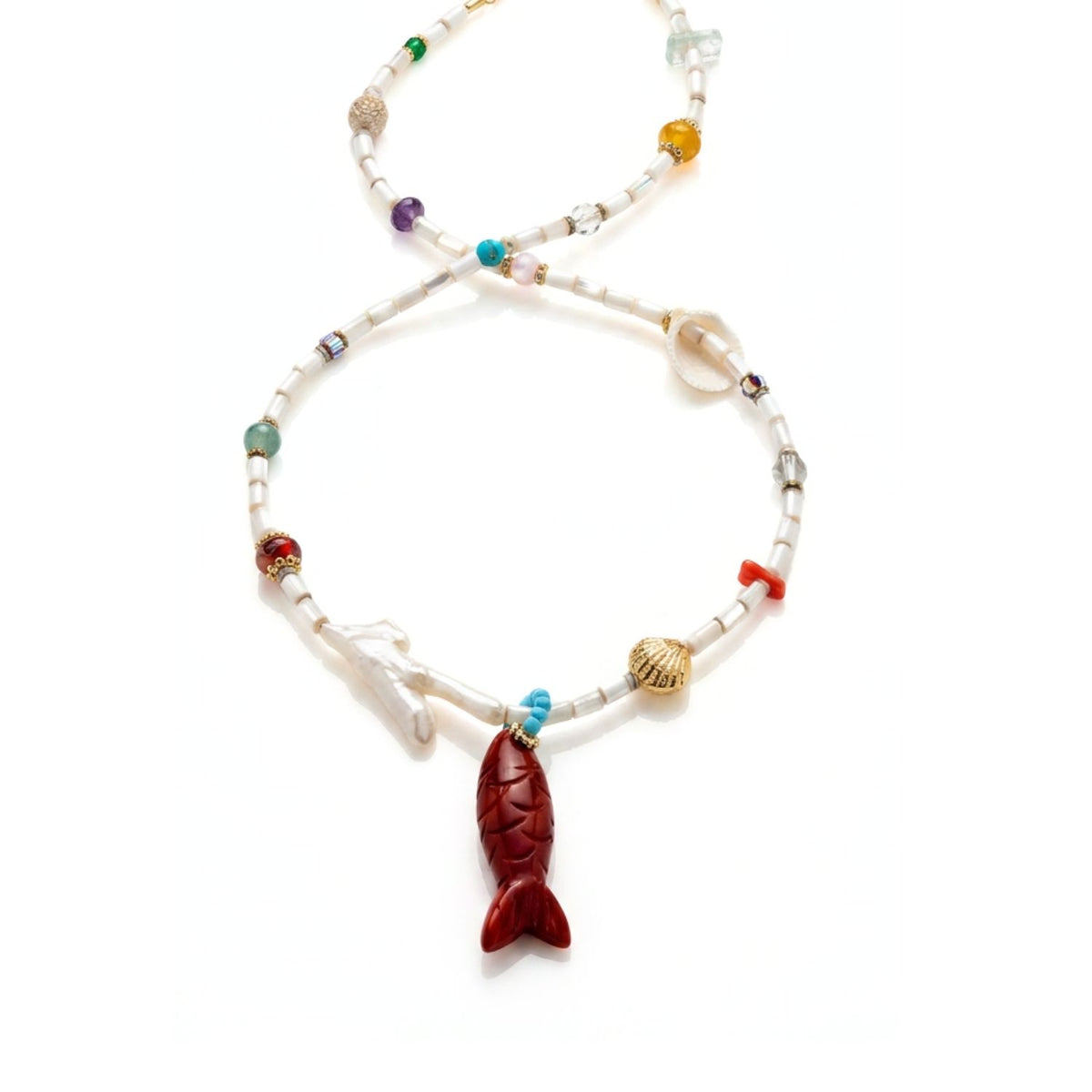 Angled studio product shot of the Marisol necklace resting on a white background, focusing on the carved Red Jasper fish pendant, coral-shaped freshwater pearl, natural shell bead, and multi-stone segment