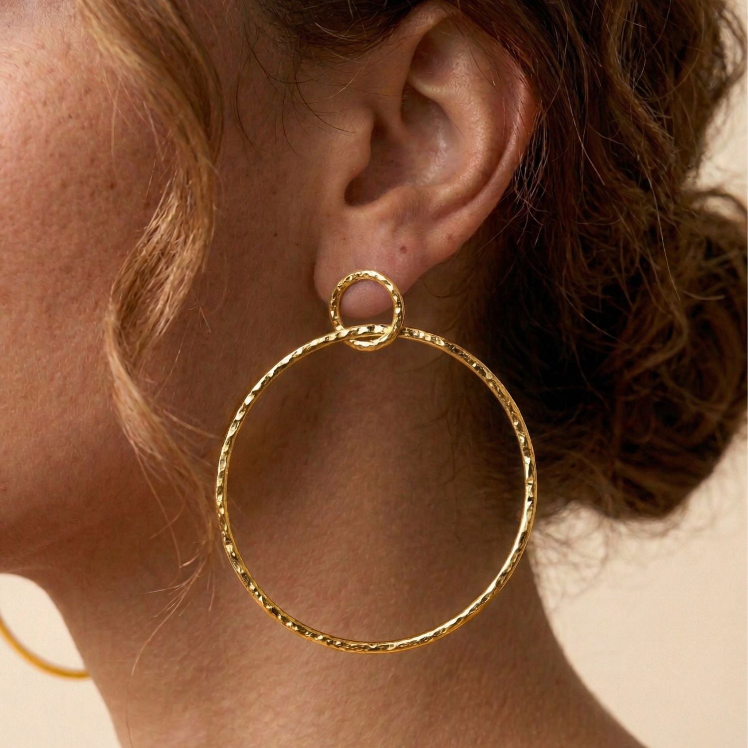 The Gold Ellen Medium Textured Hoop Post Earrings by JAREDJAMIN Jewelry Online are displayed on a plain white background, with one earring slightly higher for a modern touch, showcasing their stylish textured gold finish.