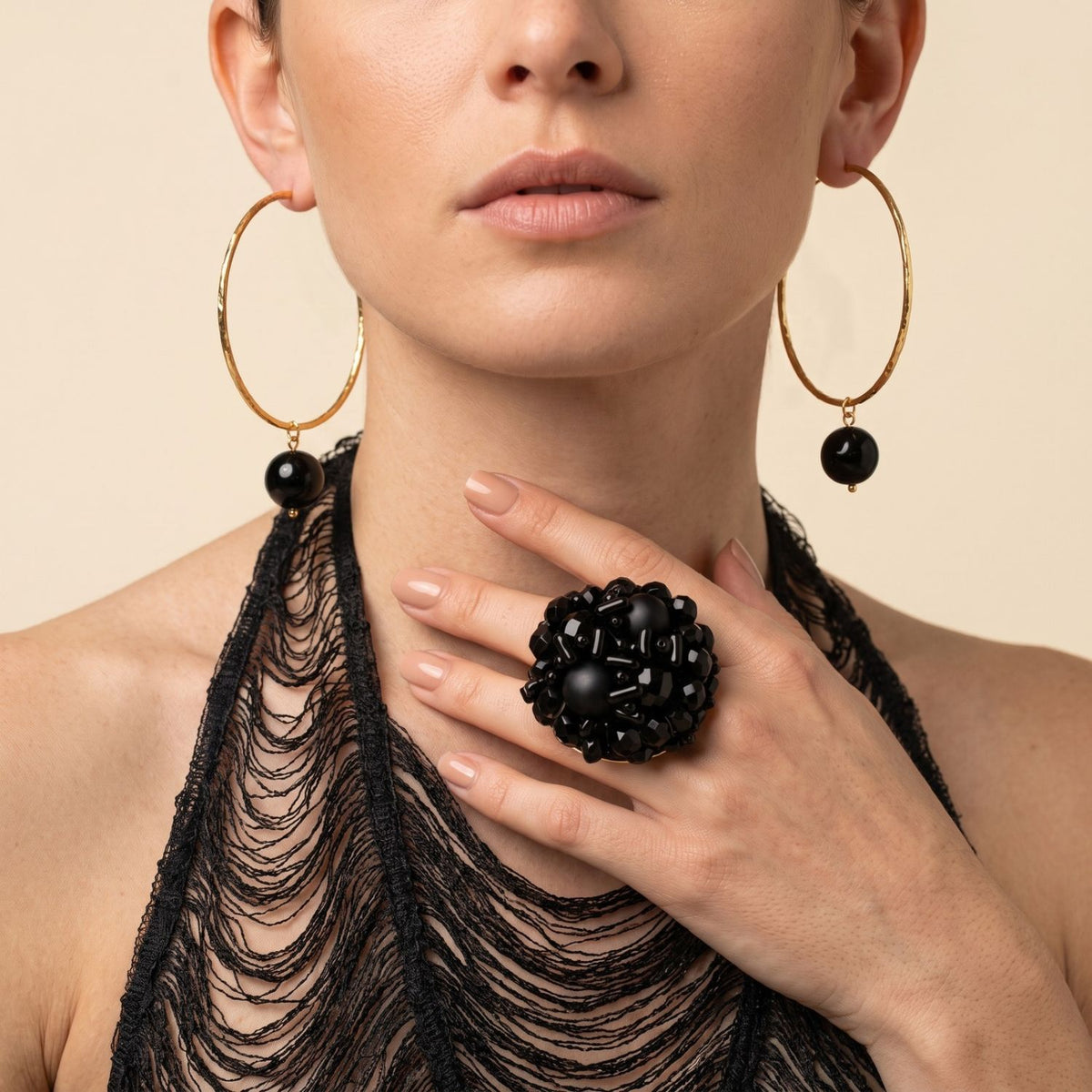 Model wearing medium gold hoop earrings, holding the black glass bead cluster cocktail ring between her fingers.