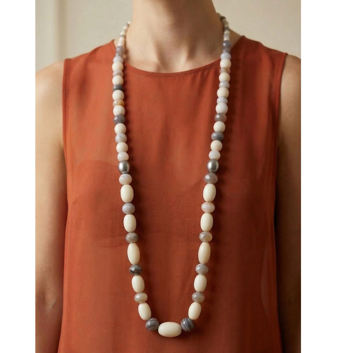 modelo usando the 43-inch Jared Jamin Montana Quarry collar, showcasing the graduated hand-knotted vintage resin, white coral, y agate beads. Los extra-long llamativo collar is styled as a dramatic single strand over a neutral outfit to highlight its sculptural texture y plata toggle clasp