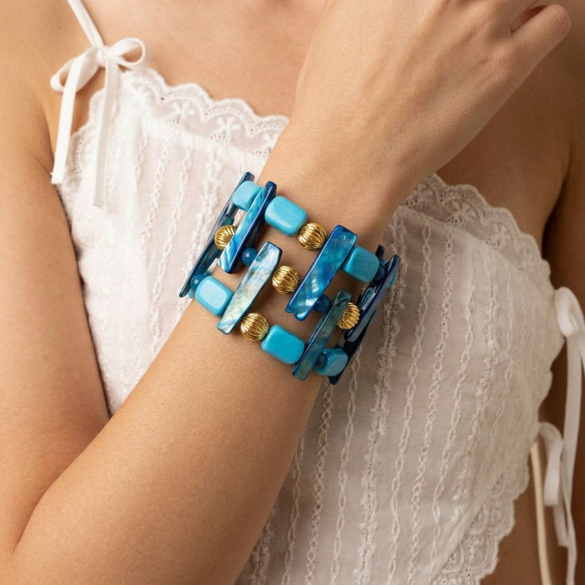 On-model shot of the 2-inch Nerida stretch cuff bracelet worn on the wrist paired with a white eyelet top, demonstrating its wide architectural fit and blue iridescent tones.