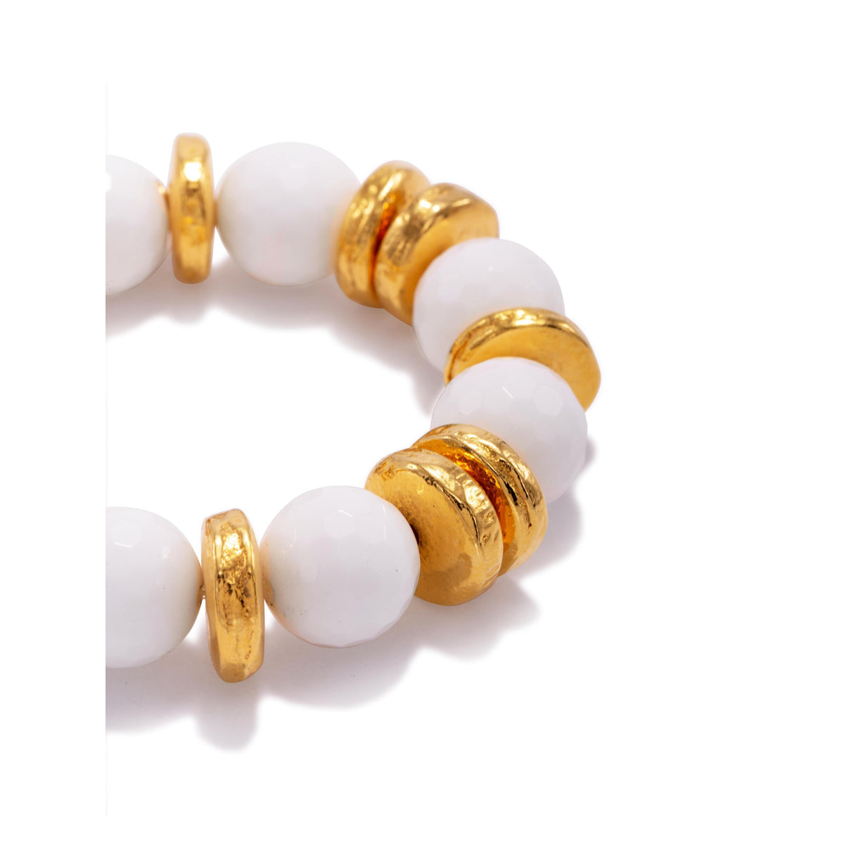 Un primer plano of the Olivia White Stretch pulsera de JAREDJAMIN Joyería Online, showing glossy white round beads alternating con brillante 18K bañado en oro disc spacers en un circular design, partially visible against a fondo blanco.