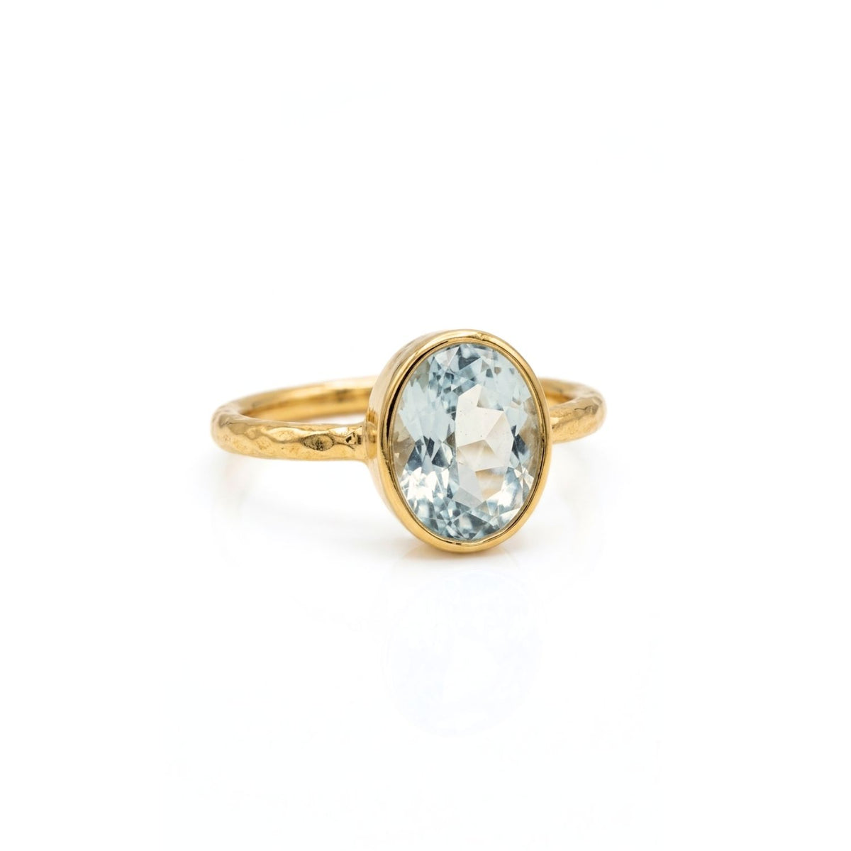 The Oval Aquamarine Gemstone Ring by JAREDJAMIN Jewelry Online features a thin, hammered gold-plated sterling silver band and a bezel-set pale blue gemstone for a simple, timeless look.