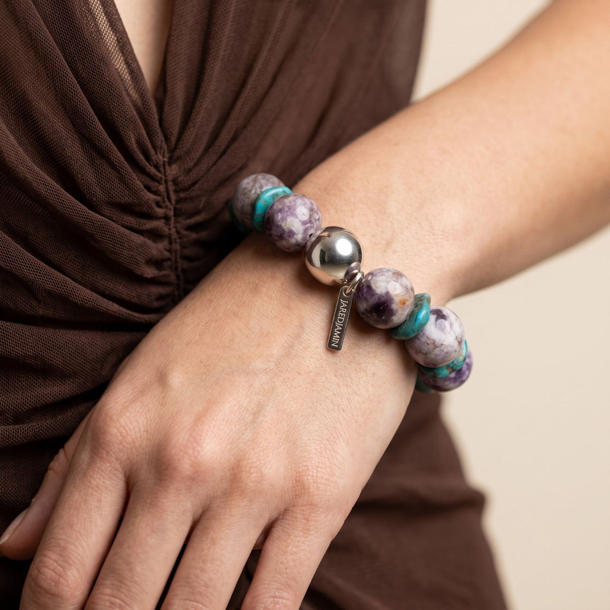 On-model shot of the Paloma Amethyst & Turquoise Howlite Stretch Bracelet worn on a wrist against a dark brown top, demonstrating its 16mm chunky gemstone scale and slip-on fit.