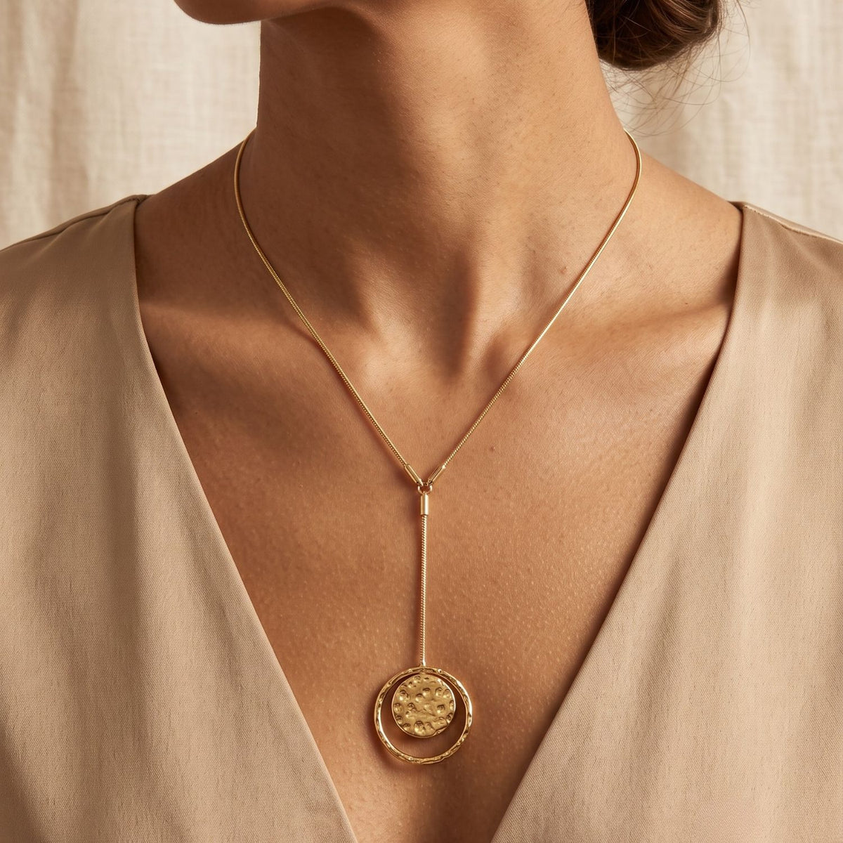 Front profile view of a model wearing the Peacock Y Pendant Necklace over a deep V-neck beige dress, demonstrating its elegant 18-inch fit and liquid-gold Y-drop silhouette.