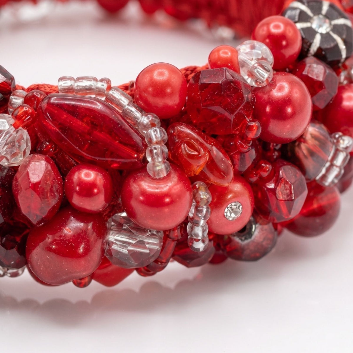Sharp macro studio shot focusing tightly on the intricate hand-embroidery of the Pomegranate Princess Bangle, highlighting the rich textural contrast between the recycled red resin beads, shiny vintage glass, and sparkling new crystals woven onto the satin base.