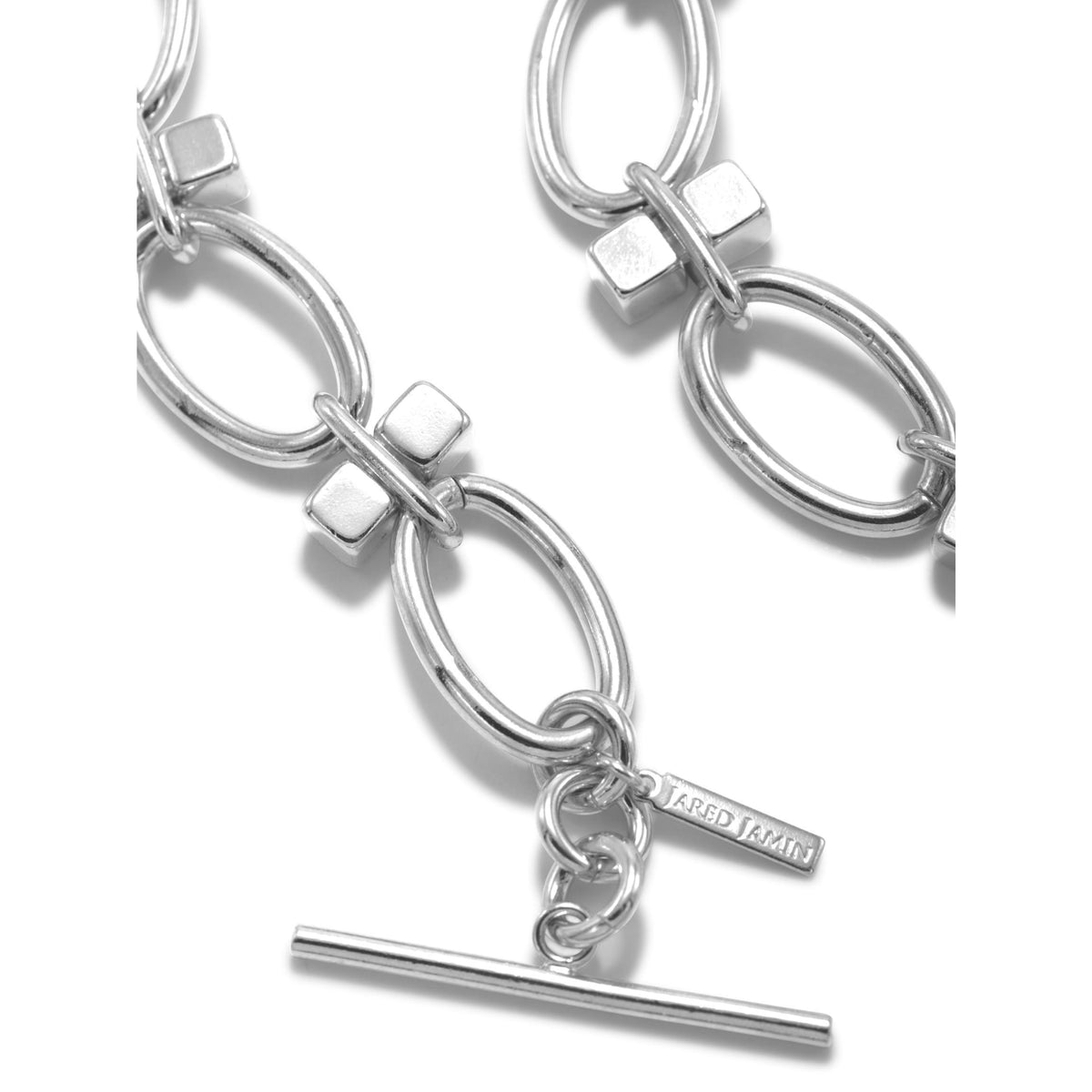 primer plano of the plata Reign Collier collar de JAREDJAMIN Joyería Online, a plata plated brass choker con large oval links, rectangular connectors, toggle clasp, y a branded tag near the clasp against a fondo blanco.
