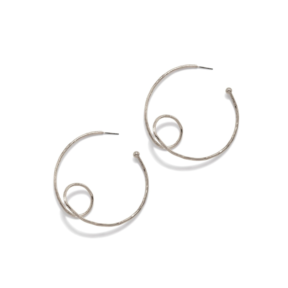 Les argent Loop-De-Loop créole Post boucles d'oreilles par JAREDJAMIN Bijoux en Ligne are argent-plated brass créoles avec a hammered texture et spiral loop detail, shown overlapping sur un fond blanc dans un modern, artistic style.