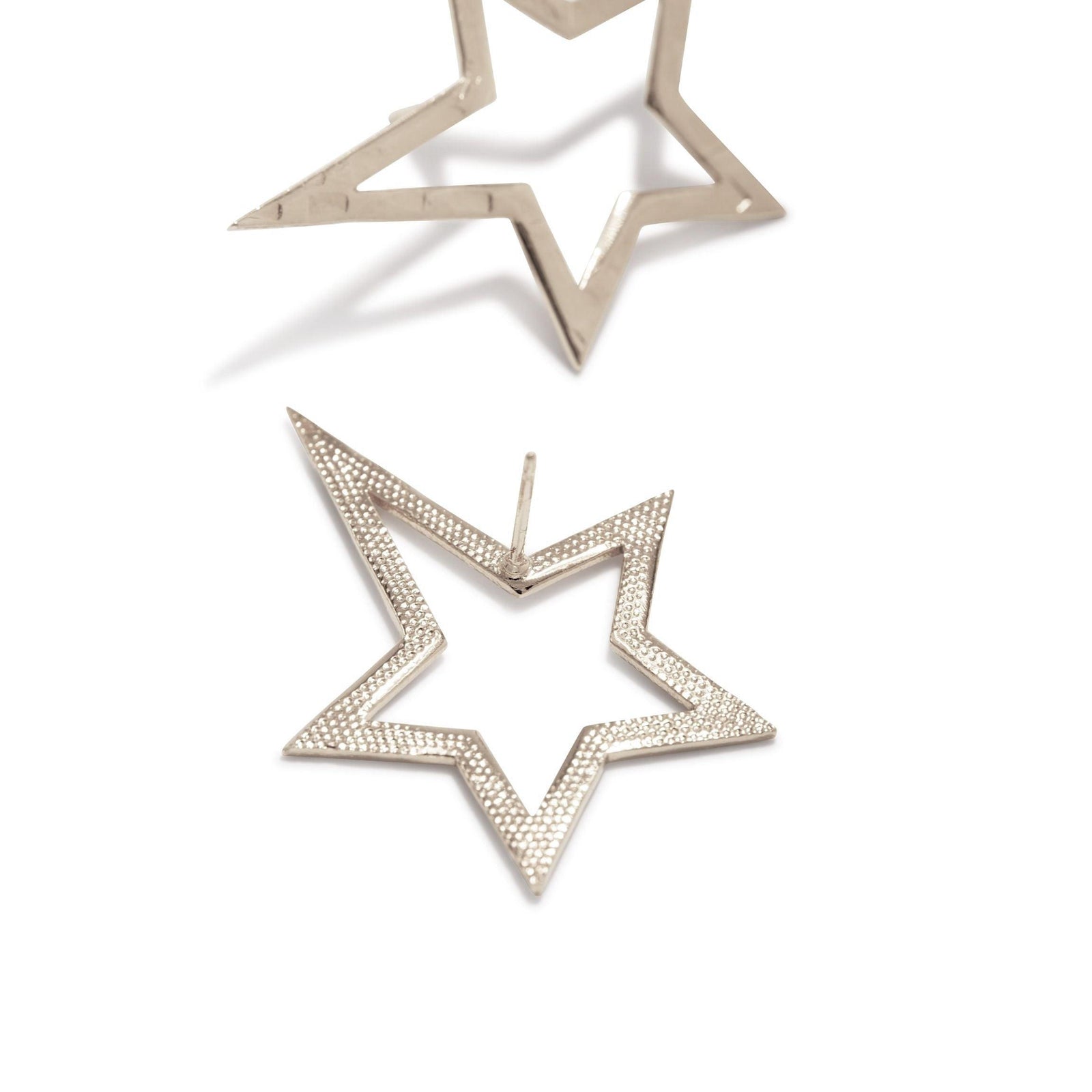 The Silver Shooting Star Dust Post Earrings Sm by JAREDJAMIN Jewelry Online are small, shiny White Bronze Plated star outline earrings with a hollow, open design, each featuring an angled five-point star against a plain white background.