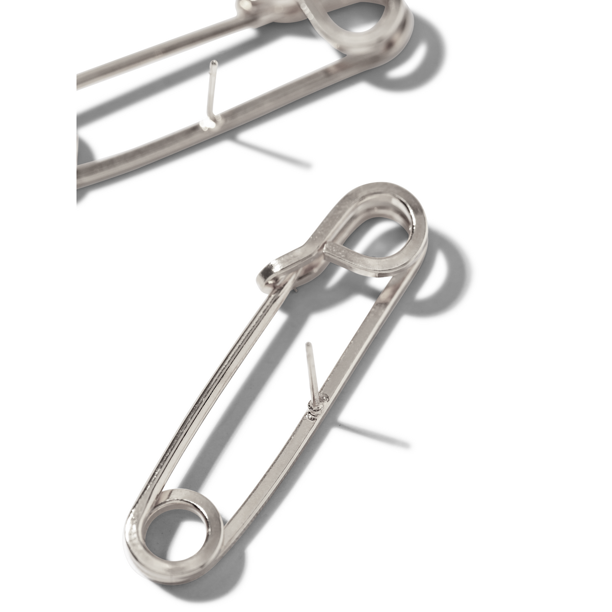 シルバー Safety First Post イヤリング JAREDJAMIN製 ジュエリーオンライン, crafted in 光沢のある, reflective metal 付きの classic punk-inspired design, are displayed open の上の ホワイト surfaceと柔らかい影.