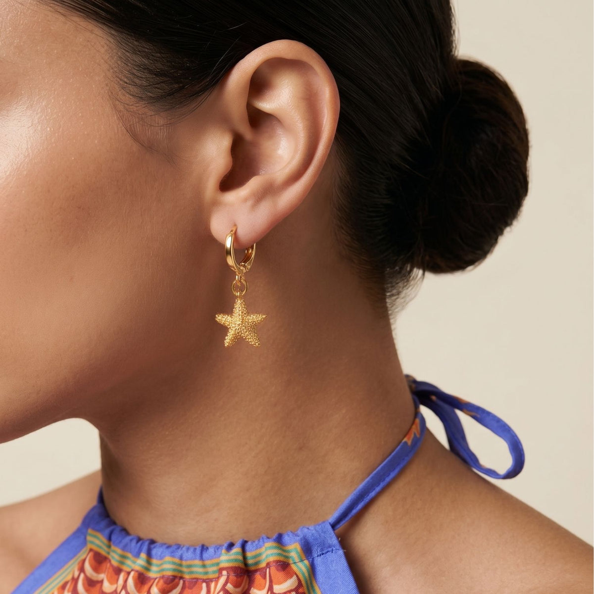 A woman with medium skin tone and a low, sculpted bun wears Sea Star Leverback Earrings—18K gold plated, hand-assembled in our West Hollywood studio. Small-batch and eco-conscious. Style Note: punctuates crisp tailoring or pared-down knits alike.