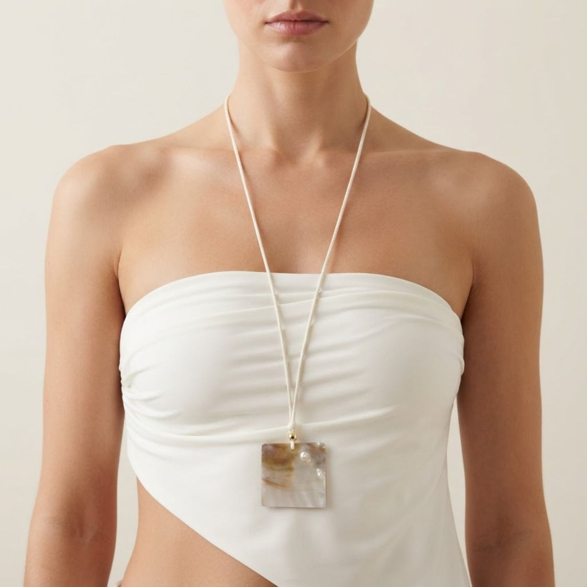 Front view of a model wearing the Maris white cord necklace adjusted long, demonstrating the dramatic drop of the square iridescent shell pendant against a white strapless top.