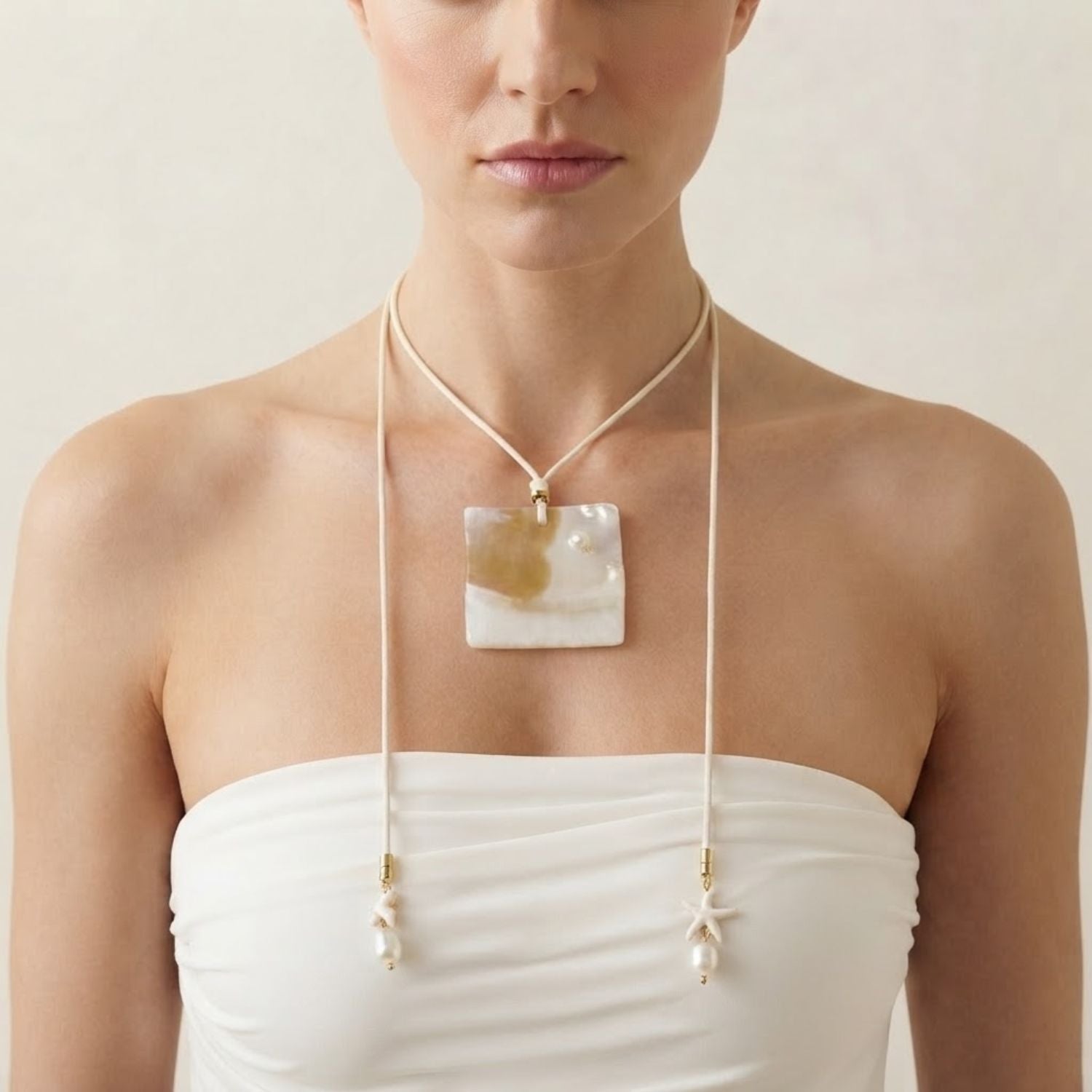 High-resolution studio product shot of the JAREDJAMIN Maris Adjustable Shell Pendant Cord Necklace on a white backdrop, showcasing the natural square shell plaque, white cordage, and pearl star tassels.