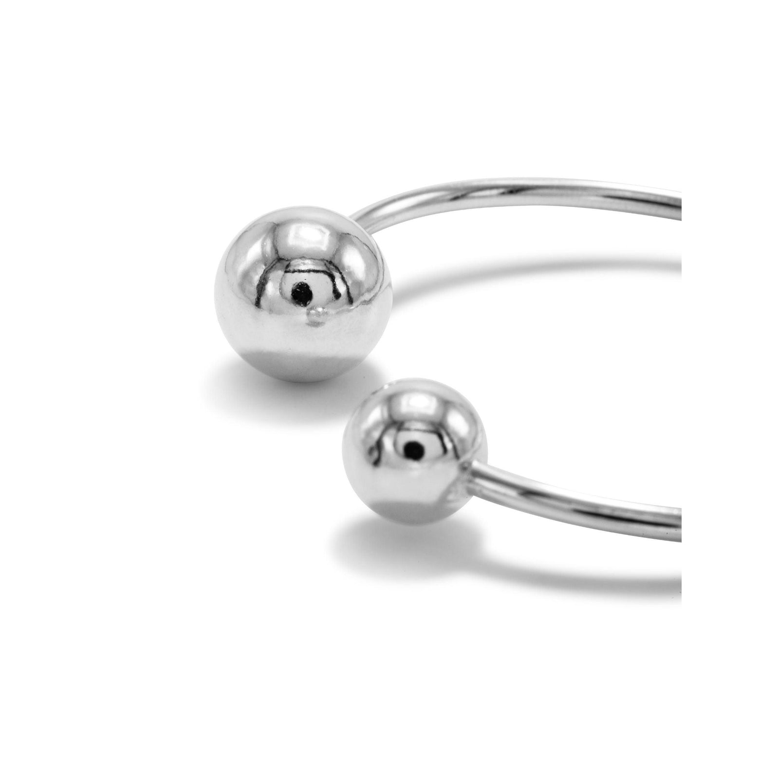 The Silver Orbita Bracelet by JAREDJAMIN Jewelry Online features a minimalist white rhodium-plated cuff with a polished finish and two rounded ball ends, shown on a plain white background to highlight its sleek, modern design.