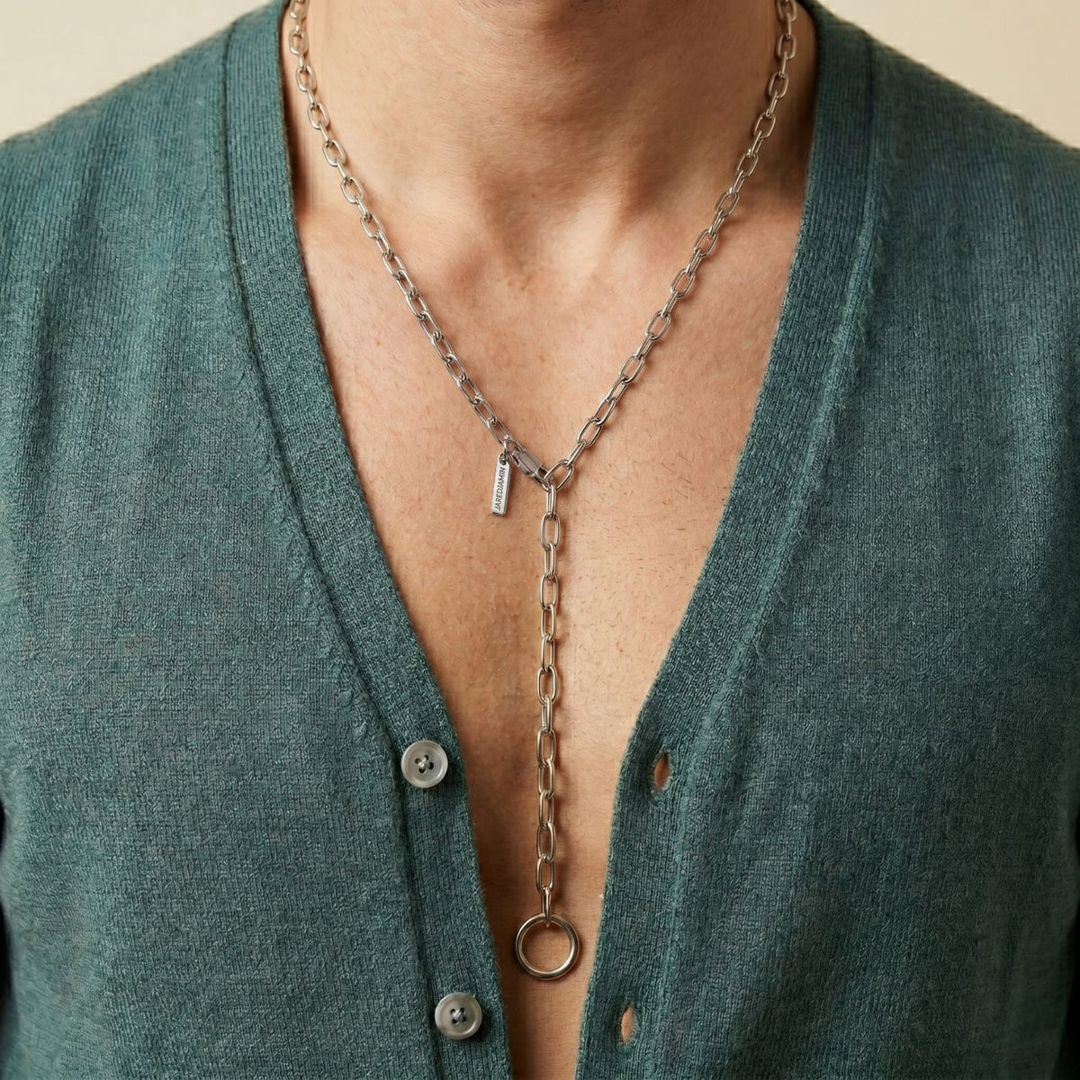 A teal V-neck cardigan frames the hand-assembled Silver Chain Reaction Necklace—vertical tag and ring pendant poised at the sternum. Cast in small batches in our West Hollywood studio using eco-conscious methods. Style Note: anchors soft knits or sharp tailoring.