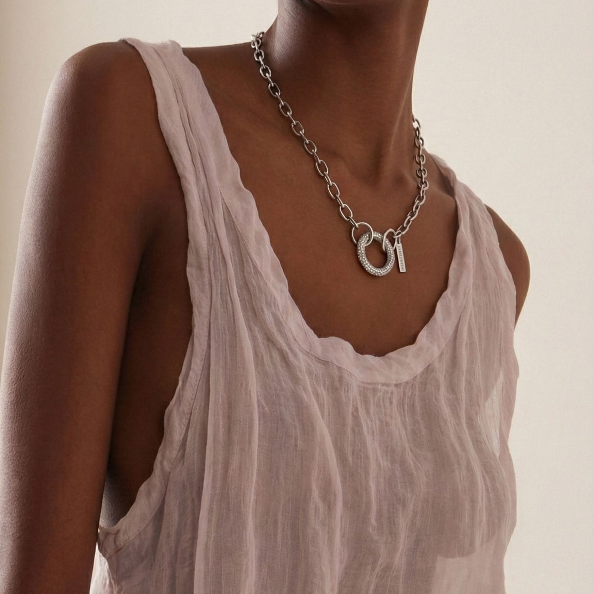 Un person models the plata Circular Pavé Clicker Clasp de JAREDJAMIN Joyería Online, styled con a sheer light pink sleeveless top, shown from shoulders to upper chest against a neutral background.