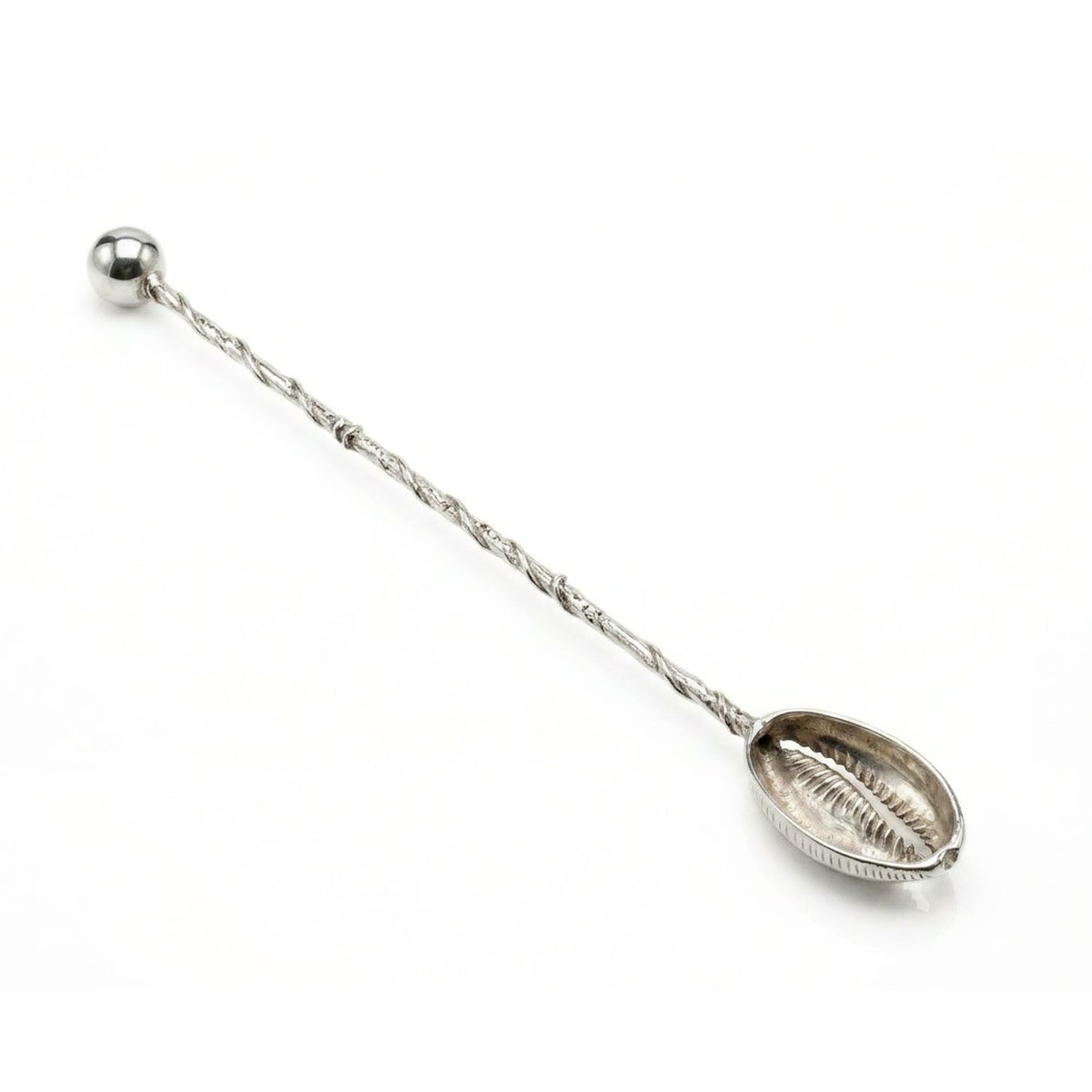 Close-up studio product shot of the silver-plated cocktail stirrer resting at a diagonal angle, highlighting the hollow interior detailing of the textured cowrie shell basin and the hand-hammered finish along the twisted wire shaft.